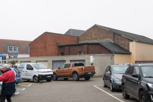 Parking lot in Schermbeck with cars and old brick industrial buildings in the background.