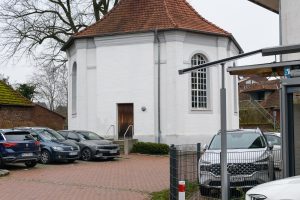 Whitewashed historic chapel in Schermbeck with red roof tiles and parked cars around.