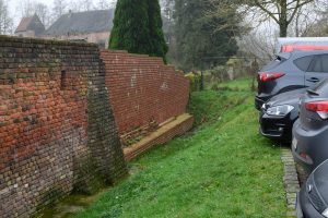 Historic brick wall in Schermbeck with green vegetation and parked cars beside it.