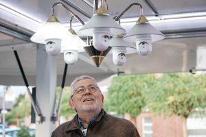 Ein älterer Mann betrachtet eine futuristische Lampe mit integrierten Überwachungskameras.