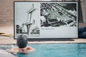 Bildschirm mit historischen Fotos des Freibads Letzigraben in Zürich, gesehen aus dem Wasser.
