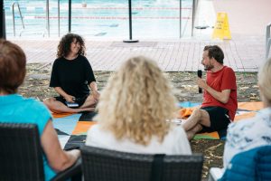 Meral Kureyshi und Julian Rauter im Gespräch auf Picknickdecken am Beckenrand des Solebads, umgeben von Zuhörer*innen.