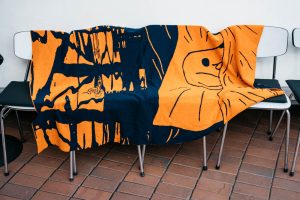 Orange and dark blue blanket with snail motif by Anna Haifisch, draped over chairs.