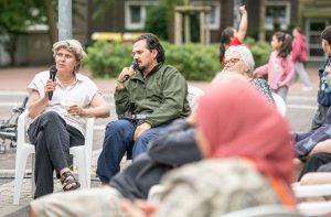 In der Gesprächsrunde sprechen Britta Peters und Driant Zeneli mit Mikrofonen vor den anwesenden Besucher*innen.
