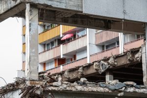 Ein Wohngebäude in Bergkamen ist hinter einer teilabgerissenen Betonstruktur zu sehen; ein pinker Sonnenschirm ragt von einem Balkon hervor.