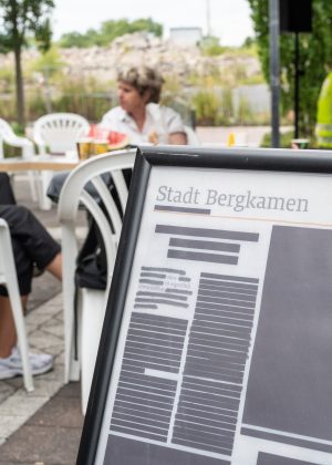 Im Vordergrund steht der Aufsteller mit dem „Local Blackout“ von Lütfiye Güzel, während im Hintergrund Besucher*innen der Grand Snail Tour sitzen.