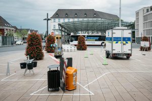 Wide-angle view of the Hammer Caretaker Championships course on Willy-Brandt-Platz, showing marked play areas, equipment stations, the mini-excavator, and a police trailer.