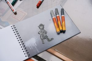 An open notebook with a drawing of a caretaker figure and several markers lies on a table at one of the activity stations.