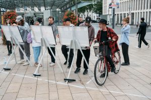 Several people work on the mounted photo boards of the course, while a man waits beside them on a bicycle.