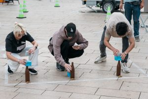 Three participants arrange or stack objects as part of one of the playful disciplines in the Hammer Caretaker Championships.