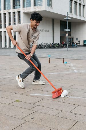 A participant sweeps a cup across the marked field using a broom during the slalom sweeping event.