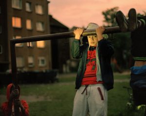 Photograph by Fatih Kurçeren: A child hangs from a metal bar on a playground while other children play nearby.
