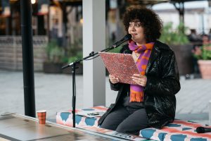 Esra Canpalat speaks into a microphone holding a manuscript during the reading.
