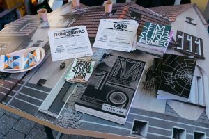 Auf einem Tisch von Nils Norman liegen Flyer und Broschüren der Grand Snail Tour und Bücher sowie Snacks von Urbane Künste Ruhr.