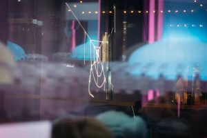 Spiegelnde Glasfront, in der die Laserlinien aus Paul Spengemanns „spin jump crawl climb dream bite hunt“ diffus reflektiert werden.