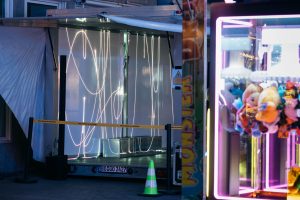 Blick in den Trailer mit der Laserinstallation „spin jump crawl climb dream bite hunt“ von Paul Spengemann; rechts daneben ein beleuchteter Greifautomat. Teile von Cem A.s Arbeit „floor pieces and stanchions“ sind sichtbar.