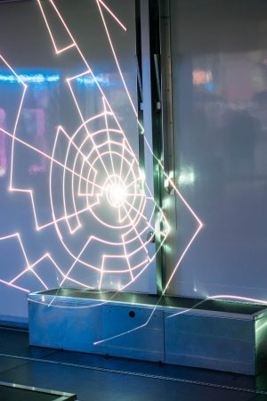 Geometrische Formen der Laserinstallation von Paul Spengemann leuchten auf der weißen Innenwand des Trailers.